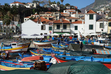 Promenade with houses, local stores and boats that are dry docked in Baía de Câmara de Lobos, Madeira, Portugal