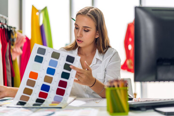 Wall Mural - Portrait of young beautiful pretty owner business woman fashion designer stylish sitting and working.Attractive young designer girl use desktop conputer and colorful fabrics at fashion workshop studio