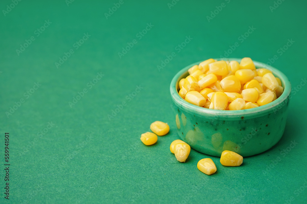 Bowl with canned corn kernels on green background