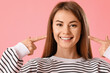 Young woman pointing at her teeth on pink background, closeup
