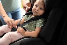 Mother Fastening Her Daughter In Child Safety Seat Inside Car