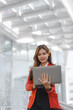 © NanSan - Using laptop, video call, Smiling young Asia business woman leader entrepreneur in red color suit working outdoor urban street walk.