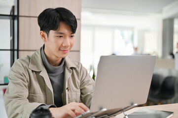 Handsome Asian male office worker or developer working on his task on laptop in the office.