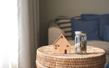 Wall Mural - A wooden house model and a glass jar of coins for saving money concept