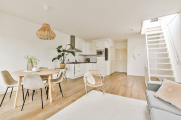 a living room with white walls and hardwood flooring, including a wooden dining table surrounded by two beige chairs