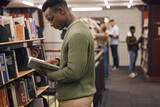 Fototapeta Panele - Black man student, reading and library with book, research and education at college to ready for exam. African gen z man, books and shelf at university for study, learning and motivation in Boston