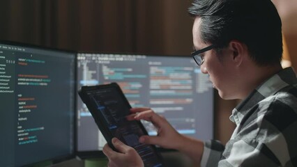 Close Up Of Asian Male Programmer Looking At Database On Tablet While Creating Software Engineer Developing App, Program, Video Game On Desktop Computer At Home
