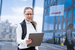 © Екатерина Переславце - Successful professional woman, in front of a glass building, holding a laptop dressed in business clothes with glasses