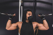 © Mdv Edwards - A masked asian man does standing overhead bicep cable curls. Wearing a black low cut tank top. Training arms at the gym.