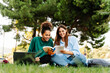 © EFStock - University student girl friends working and learning together using laptop sitting on campus grass