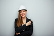 Smiling woman architect in safety helmet pointing finger at side. Isolated female portrait.