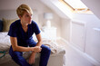 © Monkey Business - Thoughtful Woman Wearing Medical Scrubs Sitting On Bed At Home