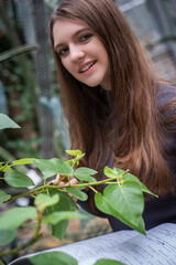 Wall Mural - Portrait of happy beautiful young science student. Youn girl in a greenhouse with tropic plants. She is studiing plants