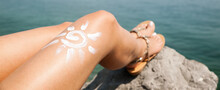 Woman Sunbathing On The Beach With A Drawing Of Sun On Her Leg  With Cream Banner Size