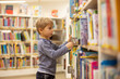 © Tomsickova - Adorable little boy, sitting in library, reading book and choosing what to lend, kid in book store.