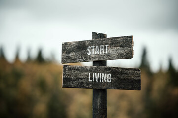 vintage and rustic wooden signpost with the weathered text quote start living, outdoors in nature. blurred out forest fall colors in the background.