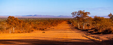 Red Dirt Road Through The Middle Of The Desert In Karijini National Park, Western Australia; Australian Outback With Red Rocks And Mountains In The Background