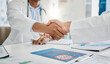 © Lou W/peopleimages.com - Closeup handshake, doctors and agreement for documents, research or health in hospital to stop virus. Doctor, shaking hands and motivation for healthcare service, wellness or teamwork goal in clinic