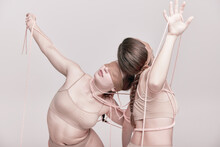 Connection. Portrait Of Two Young Girls Posing In Underwear And Ropes With Eyes Closed Over Light Studio Background. Concept Of Weird People, Contemporary Photography