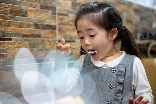 Fototapete - Happy child girl eating ice cream in white and chocolate bowl. Cute small hungry asian girl holding little spoon with chocolate ice cream for eating during lunch time
