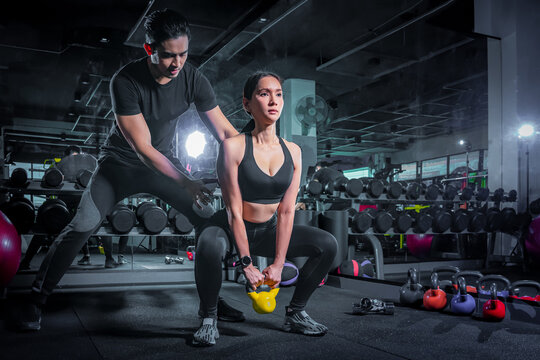 Fototapete - Young adult woman working out in gym, doing bicep curls with help of her personal trainer. Young people has workout with personal trainer in modern gym