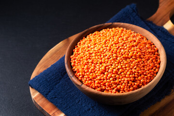 Wall Mural - Healthy food concept red lentils in wooden bowl on black background with copy space