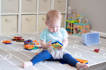 A Caucasian baby girl is playing with magnetic tiles. Child playing with toys