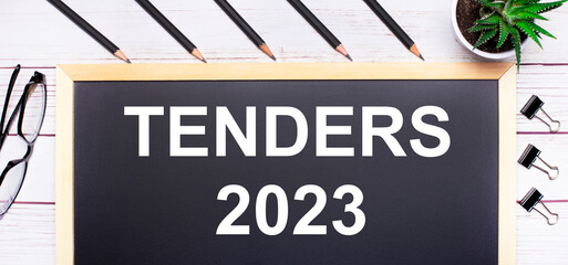 Wall Mural - On a light wooden table - a board with the text TENDERS 2023, pencils, plants, glasses and paper clips. Business concept