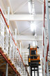 Narrow aisle high-rise stacker. Reach truck with raised cab. High height stacker loader in a industrial warehouse building with rows of racks.