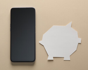 Piggy bank template cut out of white paper and smartphone on a beige background