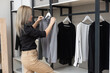 Woman choosing outfit from large wardrobe closet with stylish clothes and home stuff.