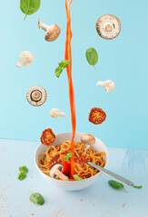 Bowl with vegan spaghetti and tomato juice, mushrooms, cauliflower and basil floating in the air against pastel blue background. Minimal creative kitchen concept of healthy food ingredients.