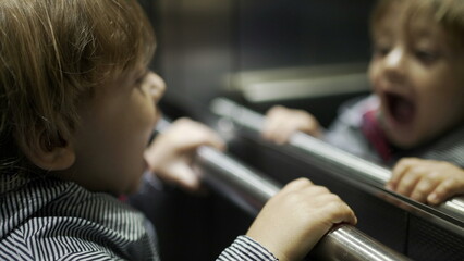 Cute baby toddler playing inside elevator staring at mirror reflection