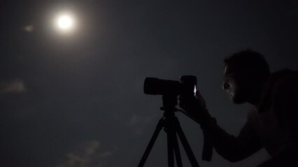 Man shooting the night cloudy sky under moon with a tripod