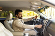 Happy arab young man businessman sitting inside luxury automobile, turning on music on dashboard before driving, handsome arabic man having car trip, side view, copy space