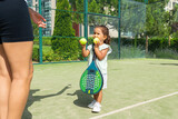 Fototapeta Młodzieżowe - Little girl handing tennis balls to her mother on a padel tennis court