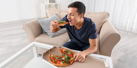 Wall Mural - Young man eating tasty pizza at home