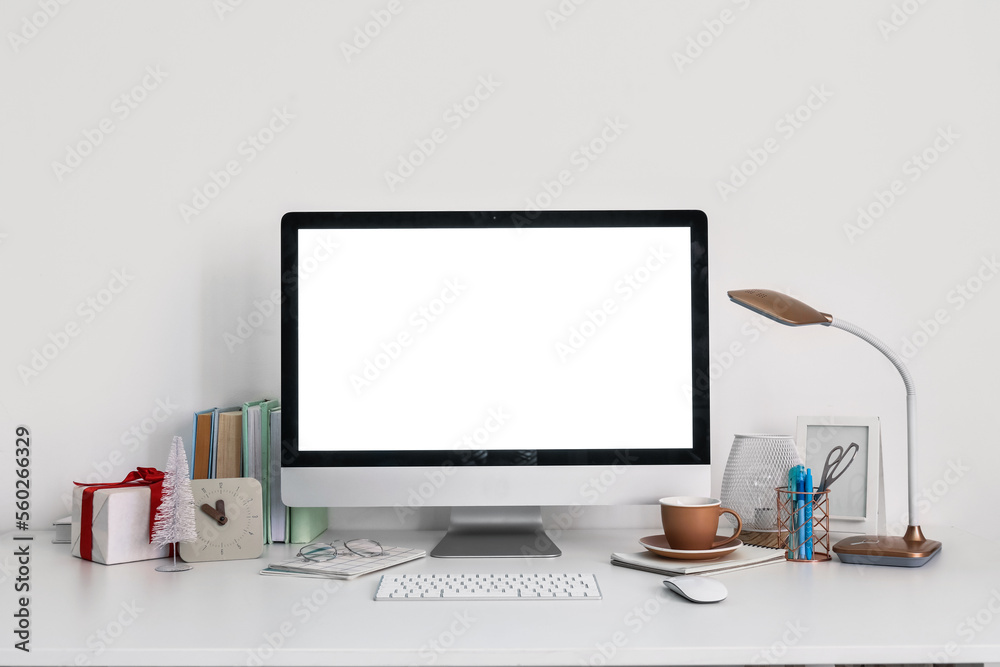 Workplace with computer, cup and Christmas gift near light wall