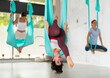 Beautiful chilean young woman hanging upside down while practicing aerial yoga during group class in modern fitness club