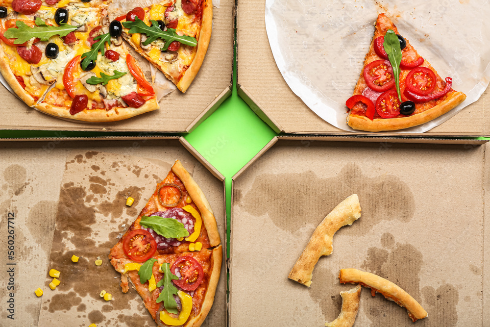 Cardboard boxes with pizza and leftovers on green background, closeup