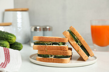 Tasty sandwiches with cucumber, cream cheese and microgreens on white table, closeup