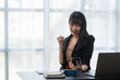 © crizzystudio - Asian businesswoman in formal suit in office happy and cheerful during using smartphone and working