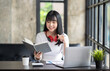 © crizzystudio - Happy Asian girl student wear wireless headphone study online with the teacher, happy young woman learn language listen lecture watch webinar write notes look at laptop sit in cafe, distance education