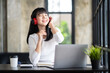 © crizzystudio - Happy Asian woman relaxing and listening to music in office with computer laptop and coffee cup. People and lifestyles concept. Freelance and outdoors workplace outdoors theme.
