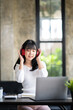 © crizzystudio - Happy Asian woman relaxing and listening to music in office with computer laptop and coffee cup. People and lifestyles concept. Freelance and outdoors workplace outdoors theme.