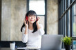 © crizzystudio - Happy Asian woman relaxing and listening to music in office with computer laptop and coffee cup. People and lifestyles concept. Freelance and outdoors workplace outdoors theme.