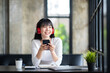 © crizzystudio - Young adult happy smiling Asian student wearing headphones talking in online chat meetings using a laptop on a university campus or at a virtual office. College female students learning remotely.