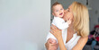 © Vera - Mom-blond kisses sweet little smiling baby-girl with blue eyes and in white t-shirt. Enjoy love, positive emotions. Happy motherhood. close up view. banner, copy space for text.