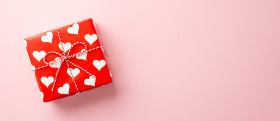 Wall Mural - Valentine's Day concept. Top view photo of giftbox in wrapping paper with heart pattern on isolated pastel pink background with copyspace