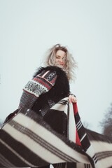 Wall Mural - Smiling woman in traditional clothes in winter portrait picture. Side view photography with gloomy grey sky on background. High quality photo for ads, travel blog, magazine, article